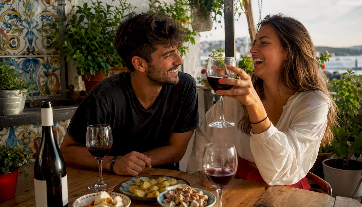 Una pareja disfruta de una copa de vino y unas tapas en la barra de un bar, compartiendo una charla relajada y el buen ambiente.