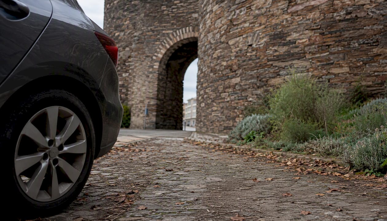 Se ve un coche aparcado parcialmente junto a la muralla romana de Lugo.