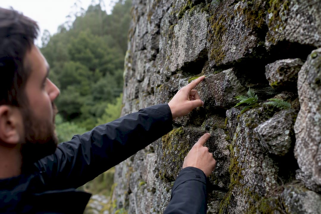 Las manos del guía señalan un detalle en el muro de piedra del castro.