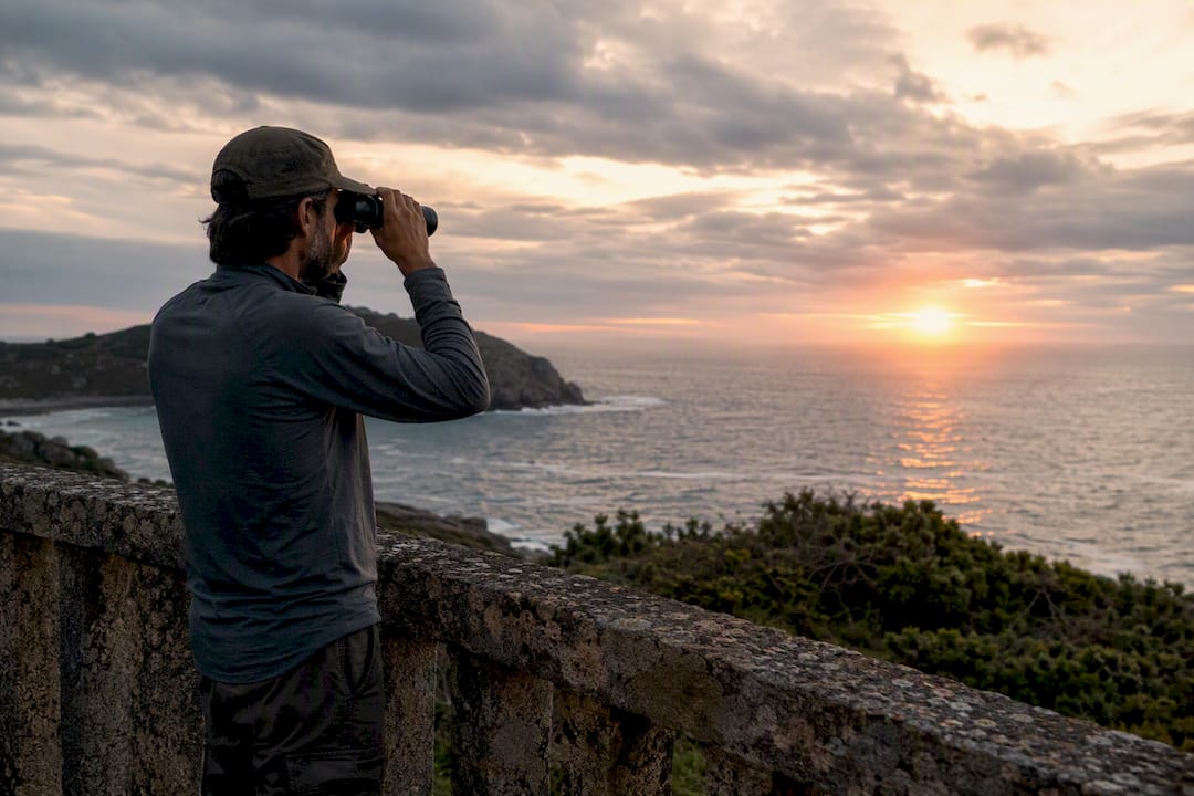 Visitante observando el mar desde un mirador costero con binoculares